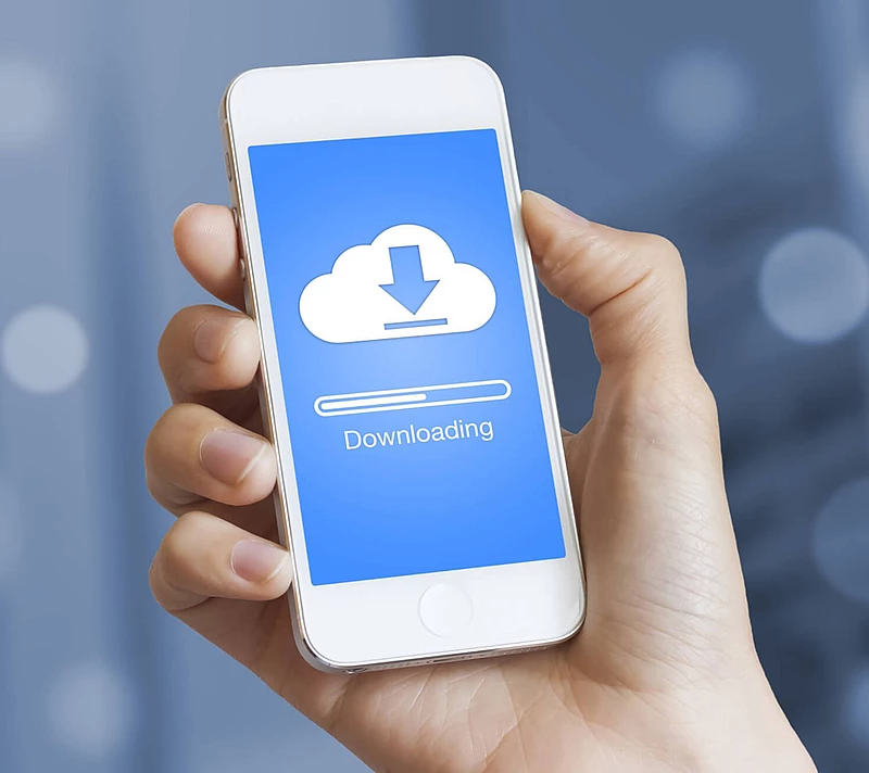 One hand is holding a cell phone that is currently downloading something.